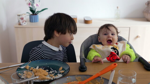 Older brother interacting with baby sibling during lunch time at home, gentle family moment showing affection, care, and playful connection between children