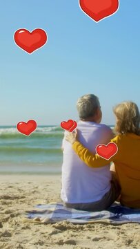 Vertical video: Seniors sitting on beach, she moving arm hugging him, loving hearts floating around