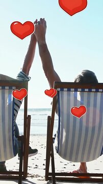Vertical video: Couple spotting moving red hearts and raising joined hands in chairs for health