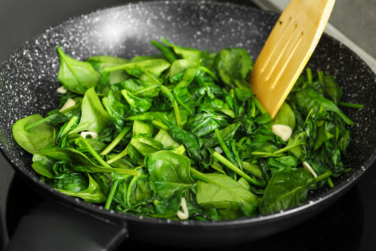 Stirring spinach and garlic with wooden spatula in frying pan, closeup