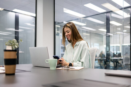 Smiling professional using phone and laptop in coworking office
