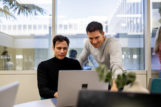 Coworkers reviewing laptop together in modern coworking office