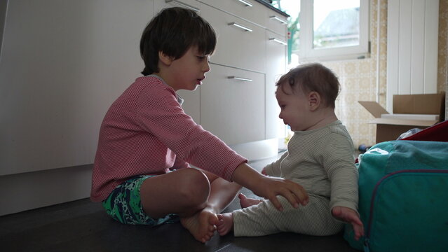 Older brother interacting with baby sibling on floor, gentle family moment showing guidance, affection, and playful bonding between siblings at home