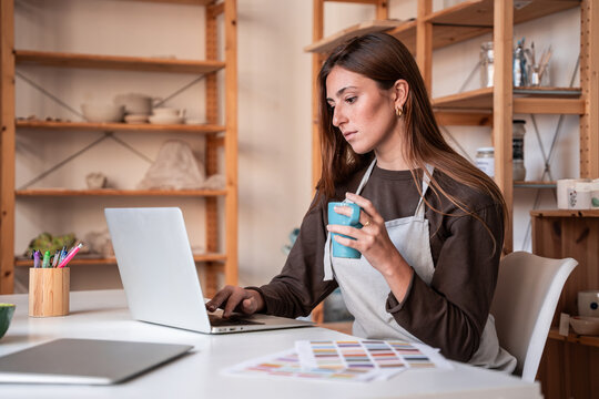Potter using laptop with coffee in pottery workshop studio