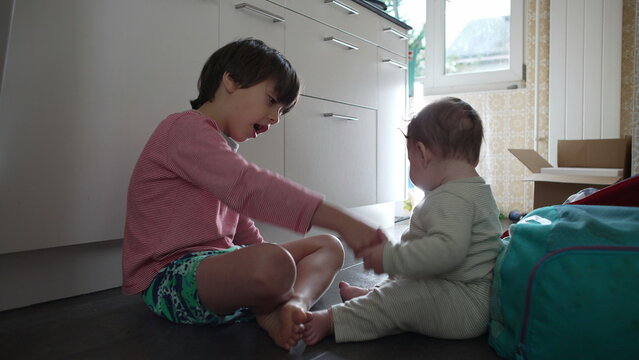 Older brother interacting with baby sibling on floor, gentle family moment showing guidance, affection, and playful bonding between siblings at home