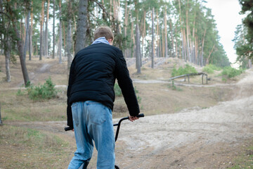 Naklejka premium Rear View of Young Man with BMX Bicycle on Sandy Forest Trail in Bike Park