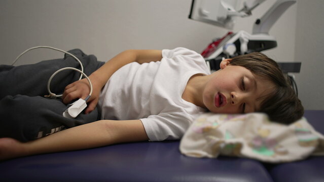 Young boy lying in hospital bed struggling to breathe during asthma attack, oxygen monitor on finger as he rests in exhaustion, emotional moment of vulnerability and medical care