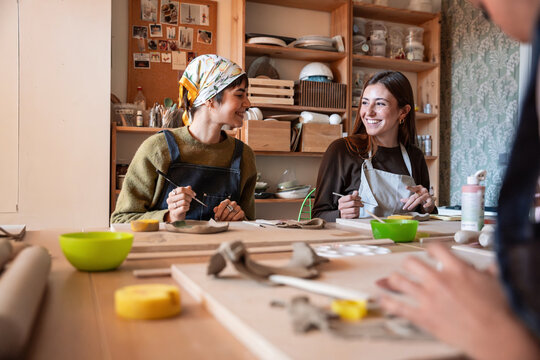 Friends shaping clay together in a cozy pottery workshop