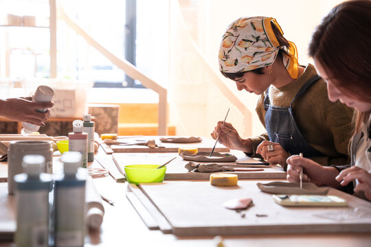 Pottery workshop students glazing clay tiles at studio table