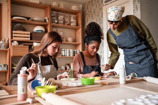 Potter teaching students painting ceramic in studio class