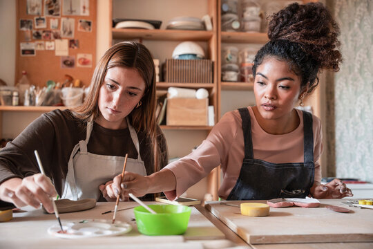 Potter teaching student to paint ceramic clay in workshop