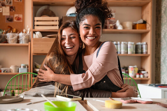 Two women hug and laugh in a pottery workshop studio