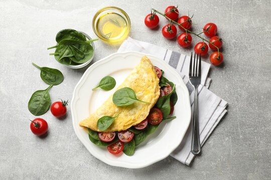 Tasty omelette with spinach and tomatoes served on light grey table, flat lay