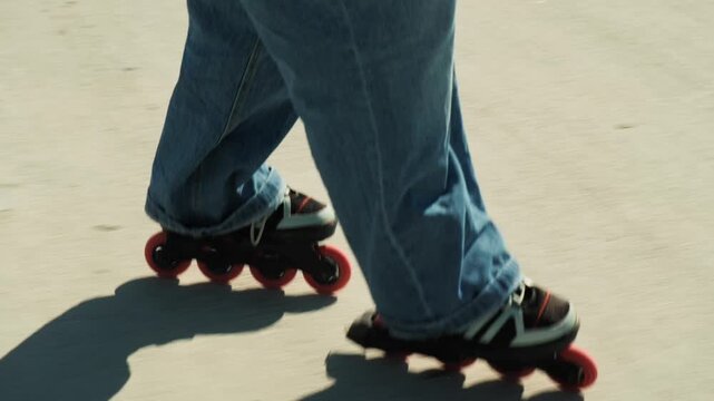 Gimbal tracking shot opening on red-wheeled inline skates gliding on sunny promenade, camera rises to reveal woman skating. Jeans, long shadow, motion blur. Dynamic urban active summer lifestyle.
