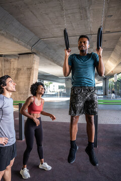 Outdoor workout friends cheering athlete doing pullup rings