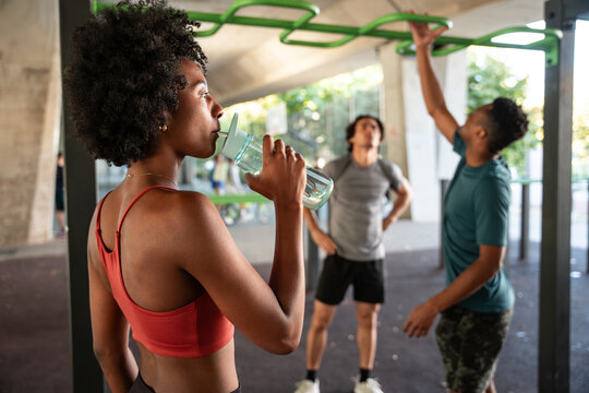 Woman drinking water while friends do outdoor workout