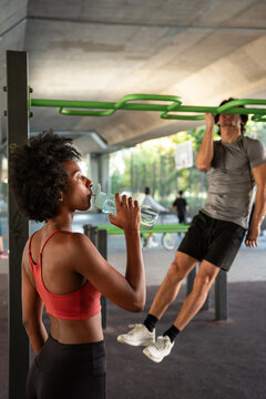 Outdoor workout break with water while man does pull up