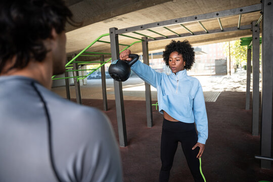 Woman training with kettlebell at outdoor gym with partner
