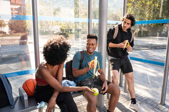 Friends eating banana at bus stop after outdoor sport
