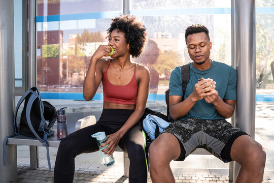 Fitness couple resting at bus stop after outdoor workout