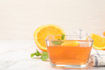 Fototapeta premium Yummy jelly in glass bowl, oranges and mint on white marble table, closeup. Space for text