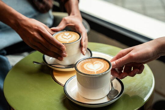 Sharing latte art coffee at cafe table by window