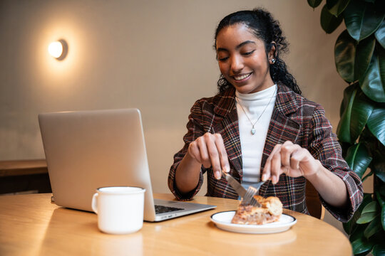 Young woman eating dessert while working on laptop