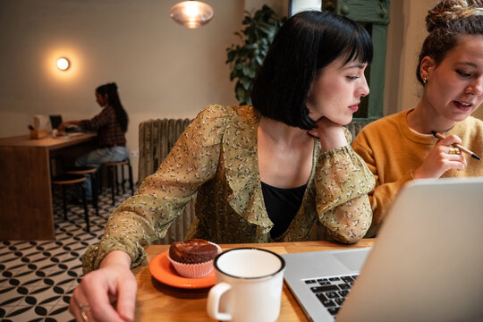 Two friends working on laptop together in cozy cafe