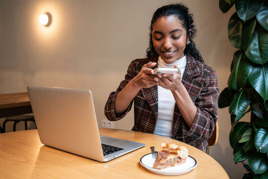 Young woman texting by laptop while eating dessert at cafe