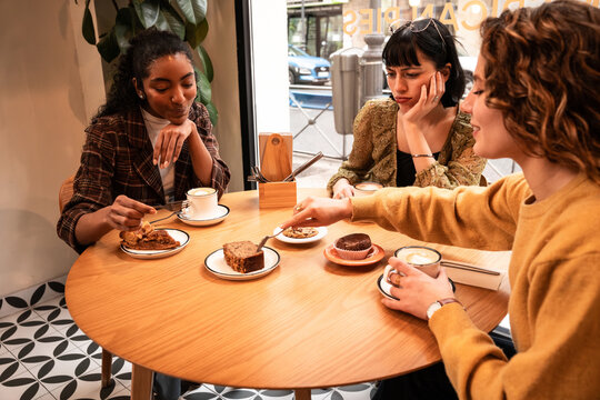 Multiethnic friends sharing cake and coffee in cafe