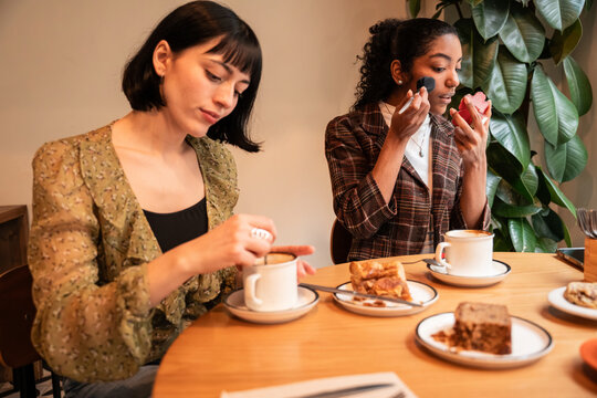 Multiethnic friends applying makeup while having coffee