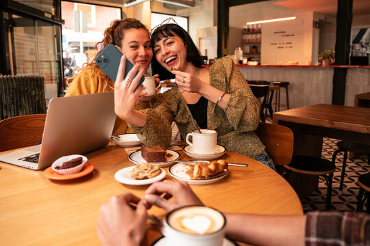Friends taking a selfie at cafe table with coffee and cake