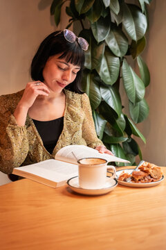 Woman reading a book at cafe with coffee and pastry
