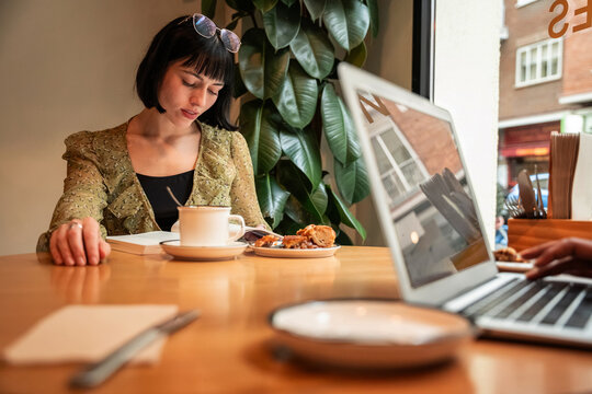 Woman working in cafe with laptop, coffee and pastry