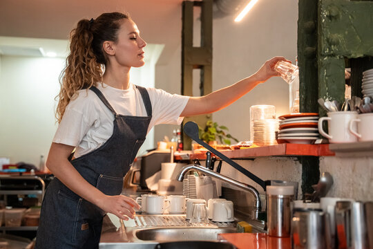 Female barista washing glassware behind cafe counter