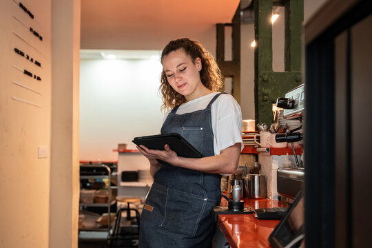 Young barista using tablet at coffee shop counter