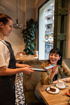 Waitress taking mobile payment from customer in caf&eacute;