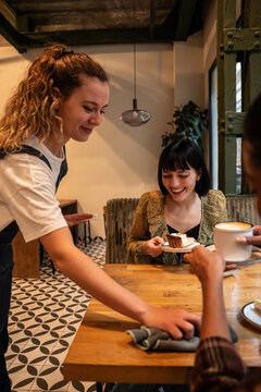 Friendly waitress serving cake and coffee in cozy cafe