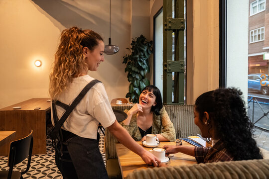 Friendly barista serving coffee to multiethnic friend
