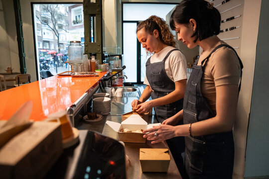 Two cafe staff packing takeaway order at busy counter