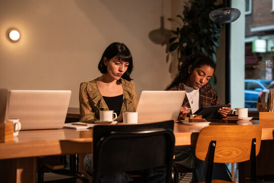 Multiethnic women working on laptop and tablet in cafe