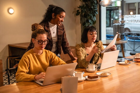 Multiethnic women collaborating on laptop work in cafe