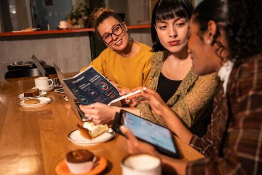 Multiethnic colleagues reviewing report and tablet at cafe