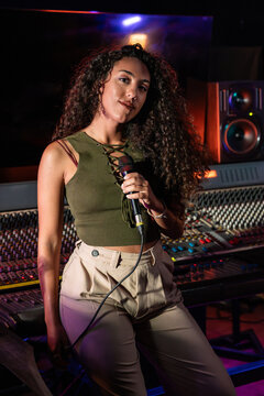 Young vocalist holding microphone in music studio control room