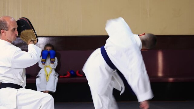 An athlete performs circular kicks on a machine held by a trainer