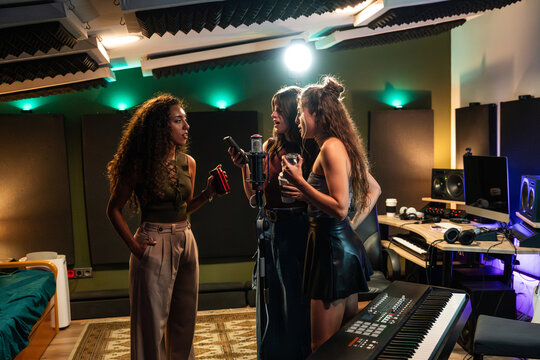 Three young women recording vocals in a modern music studio