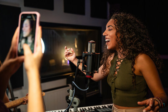 Woman singing in recording studio while friend films