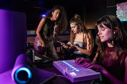 Women recording vocal and mixing music in studio at night