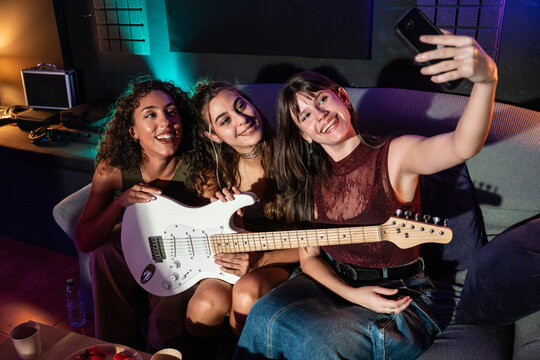 Friends taking selfie with electric guitar on studio sofa