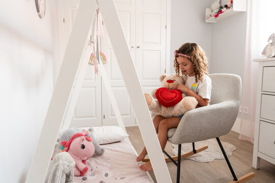 Girl hugging teddy bear in cozy nursery reading corner